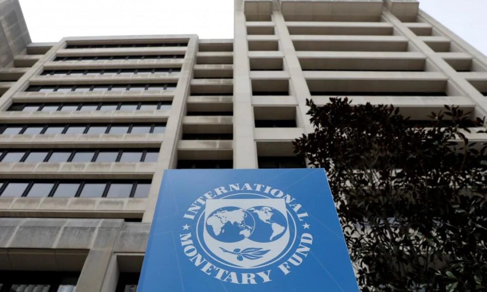 Tall concrete office building with a blue International Monetary Fund banner in the foreground, featuring the IMF globe logo and text.