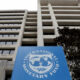 Tall concrete office building with a blue International Monetary Fund banner in the foreground, featuring the IMF globe logo and text.
