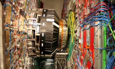 Inside a high-tech lab, a large circular magnet ring with blue and orange cables and metal support structures surrounding it.
