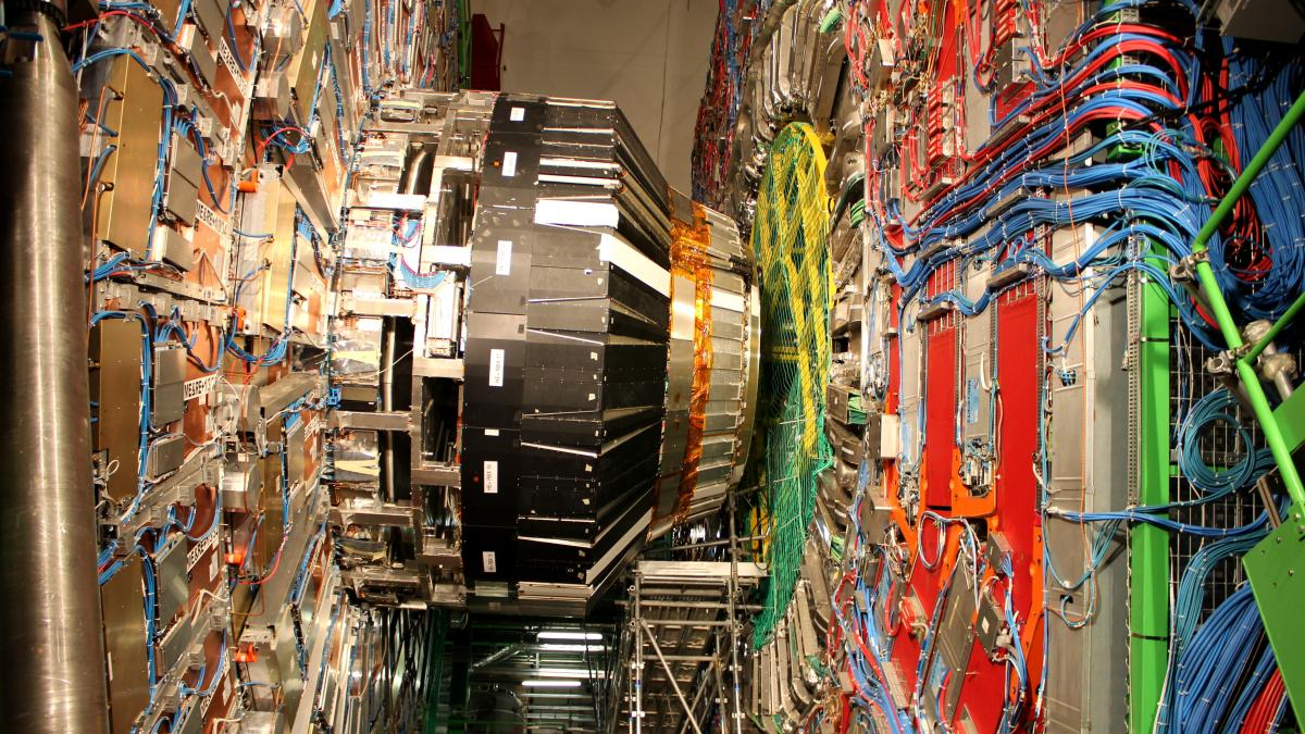 Inside a high-tech lab, a large circular magnet ring with blue and orange cables and metal support structures surrounding it.