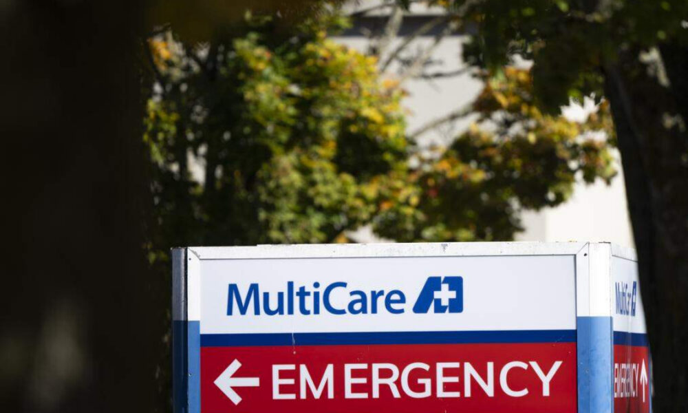MultiCare sign with a blue medical cross and a red EMERGENCY banner pointing left, outdoors.