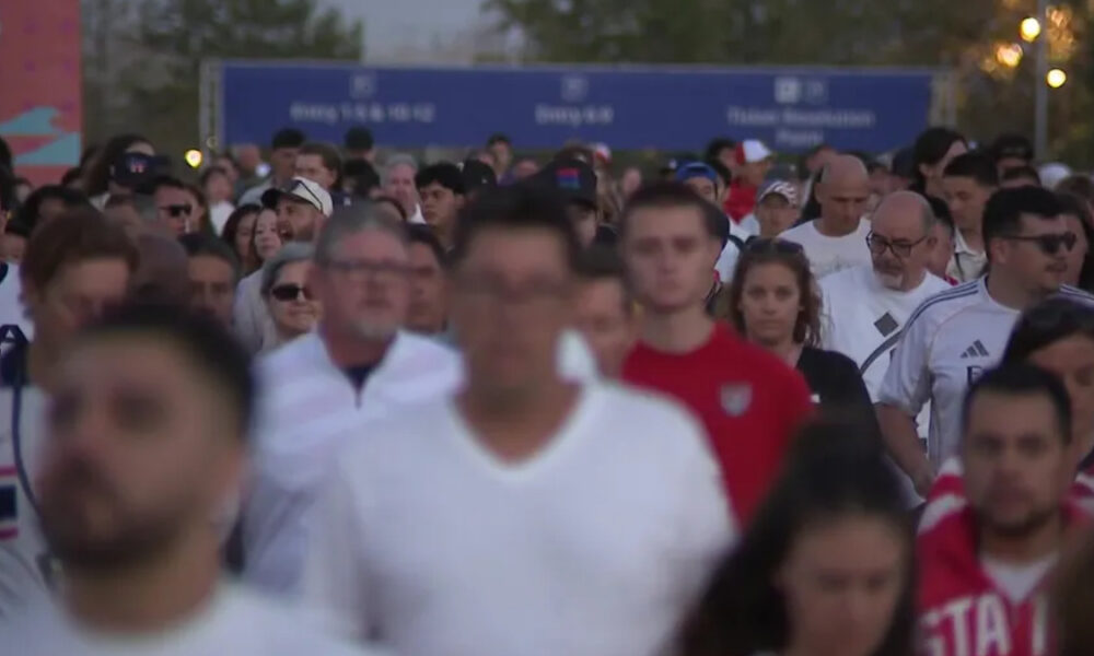 Crowd of runners at the start of a race, facing the camera, with blue banners overhead in the background.