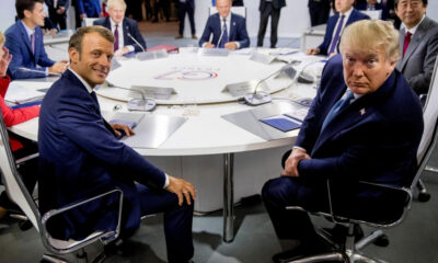 Two men in suits sit at a round conference table during a formal international meeting.