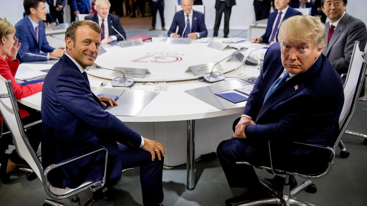 Two men in suits sit at a round conference table during a formal international meeting.