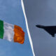 Irish flag waving on a flagpole on the left, a bomber jet in flight on the right, divided by a curved white line.