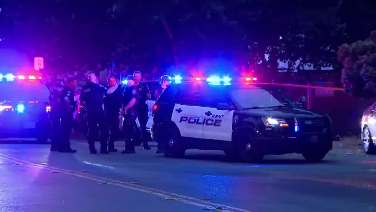 Nighttime street scene with Kent Police patrol SUV and multiple officers near flashing blue and red lights behind a taped area.