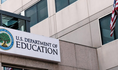 Sign for the U.S. Department of Education on a modern office building with an American flag nearby