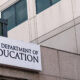 Sign for the U.S. Department of Education on a modern office building with an American flag nearby