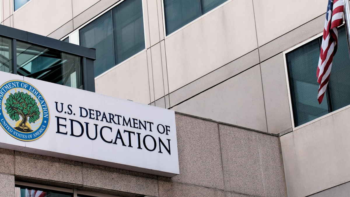 Sign for the U.S. Department of Education on a modern office building with an American flag nearby