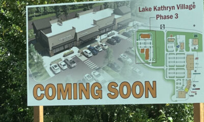 Signboard advertising Lake Kathryn Village Phase 3, showing a rendered shopping center, parking lots, and a map with a large 'COMING SOON' text at the bottom.