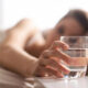 Person lying in bed reaching for a glass of water on a bedside table.
