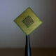 Close-up of a green square CPU with gold contact pins arranged in a grid, mounted on a black stand.