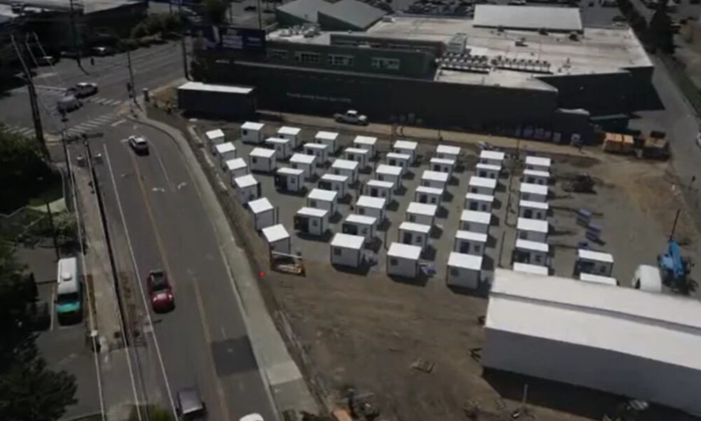 Aerial view of a temporary lot with rows of white modular buildings beside a large gray commercial building.