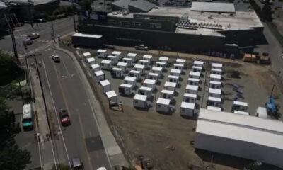 Aerial view of a temporary lot with rows of white modular buildings beside a large gray commercial building.