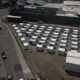 Aerial view of a temporary lot with rows of white modular buildings beside a large gray commercial building.