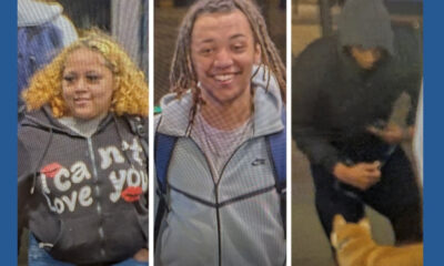 Three young people walking side by side: left with curly blond hair in a hoodie, middle smiling with braids and a gray jacket, right in a dark hoodie with a dog at their feet in the frame.