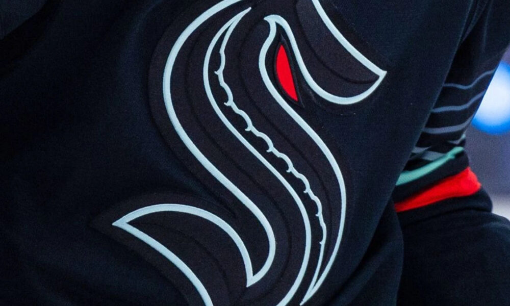 Close-up of a black garment with a stylized white serpentine logo and a red eye mark on the fabric edge.