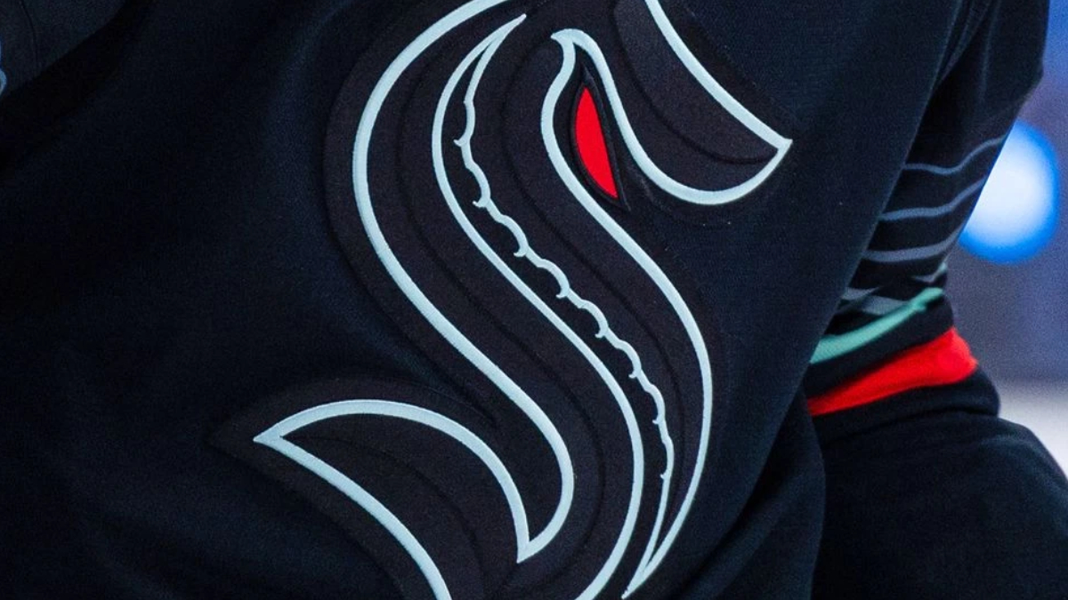 Close-up of a black garment with a stylized white serpentine logo and a red eye mark on the fabric edge.