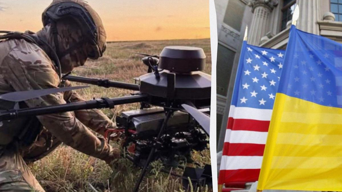 Soldier in camouflage crouches beside a mounted weapon in a grassy field at sunset, with US and Ukrainian flags nearby.
