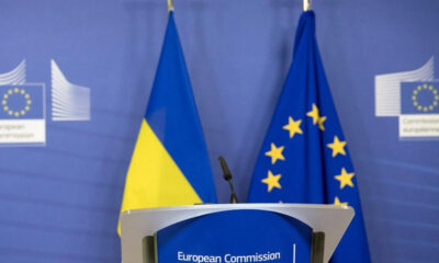 Podium at a European Commission press event with Ukrainian and EU flags in the background.