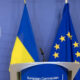 Podium at a European Commission press event with Ukrainian and EU flags in the background.