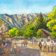 Bustling mountain village square with outdoor cafes, pedestrians, and families against a backdrop of green hills and distant mountains.