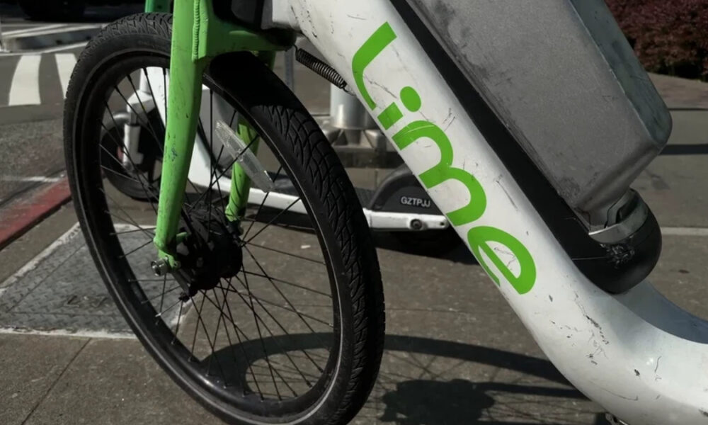 Close-up of a Lime bike-sharing bicycle's front wheel and green frame with the Lime logo on a sidewalk.
