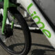 Close-up of a Lime bike-sharing bicycle's front wheel and green frame with the Lime logo on a sidewalk.
