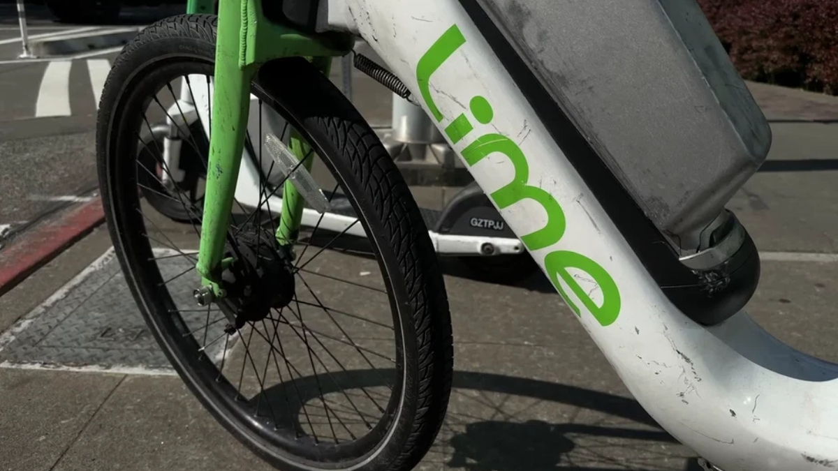 Close-up of a Lime bike-sharing bicycle's front wheel and green frame with the Lime logo on a sidewalk.