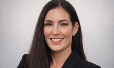 Professional headshot of a smiling woman with long dark hair wearing a black blazer and pearls against a neutral background.