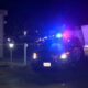 Police cars with blue and red lights at night in a residential area, yellow tape cordoning off the scene.