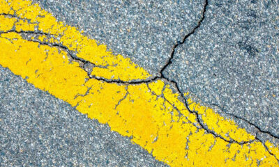 Cracked asphalt with a bold yellow road line running diagonally across the image.