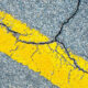 Cracked asphalt with a bold yellow road line running diagonally across the image.