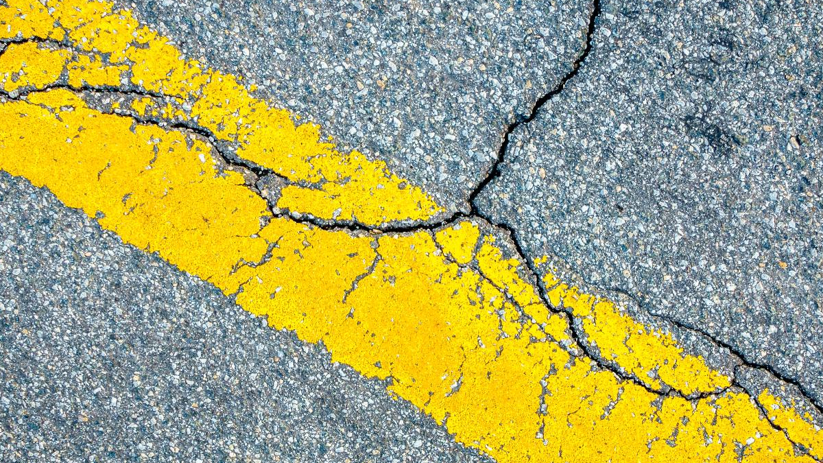 Cracked asphalt with a bold yellow road line running diagonally across the image.