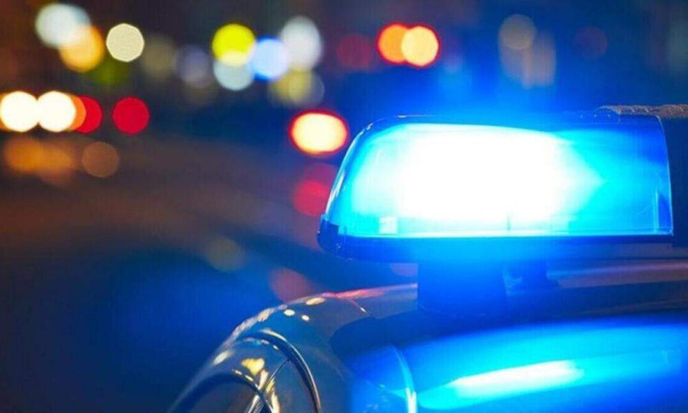 Police car with blue emergency lights flashing at night; blurred city lights in background.