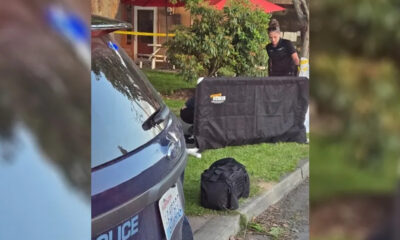 Police SUV with yellow tape; investigator behind a large black privacy screen near equipment on the grass and curbside.
