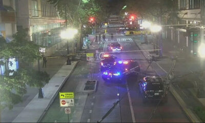 Nighttime city street blocked by police with multiple emergency vehicles and flashing lights in the distance.