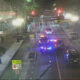 Nighttime city street blocked by police with multiple emergency vehicles and flashing lights in the distance.