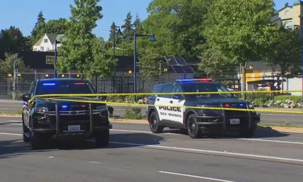 Two police SUVs with flashing blue and red lights cordon off a street with yellow crime tape across the road.