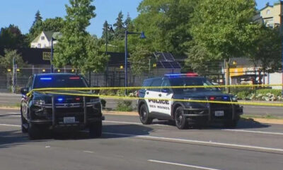 Two police SUVs with flashing blue and red lights cordon off a street with yellow crime tape across the road.