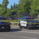 Two police SUVs with flashing blue and red lights cordon off a street with yellow crime tape across the road.