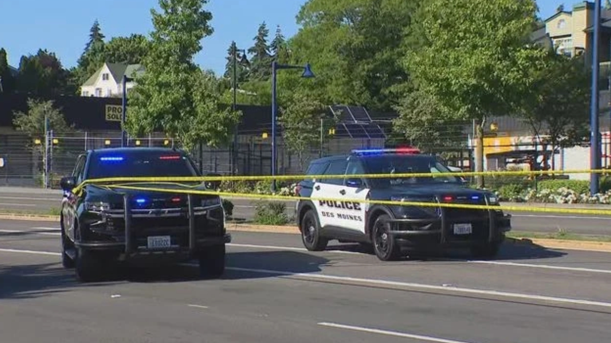 Two police SUVs with flashing blue and red lights cordon off a street with yellow crime tape across the road.