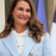 Smiling woman in a light blue blazer outdoors, with flags in the background, posing for a formal photo.
