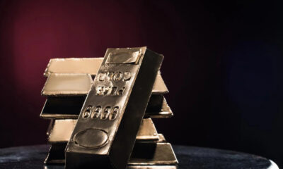 Stack of gold bars on a dark reflective surface with a reddish glow in the background, conveying wealth and precious metal storage