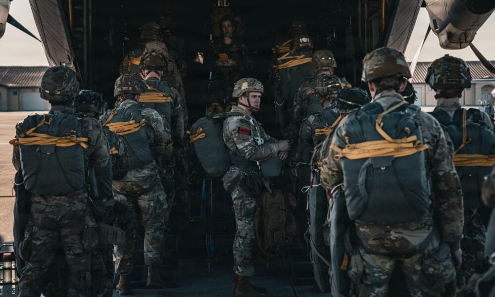 Soldiers in camouflage with backpacks lining up to board a large military transport aircraft via its open rear ramp.