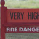 Red fire danger sign with bold 'VERY HIGH' on top and 'FIRE DANGER' below, outdoors in a grassy area.