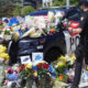 Police SUV covered with flowers, notes, and balloons in a memorial scene; a uniformed officer stands nearby.