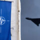 Blue banner displaying the NATO emblem (compass rose) hanging on a stone wall left side; right side shows a flying B-2 Spirit stealth bomber against a cloudy sky