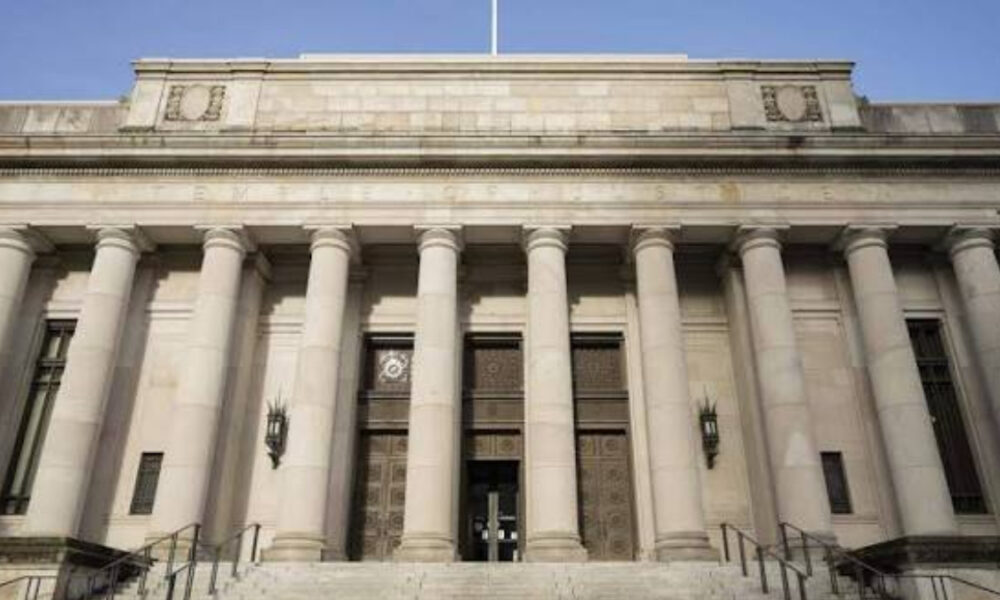 Front view of a grand neoclassical building with tall stone columns and a central double door entrance on steps.
