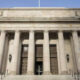 Front view of a grand neoclassical building with tall stone columns and a central double door entrance on steps.